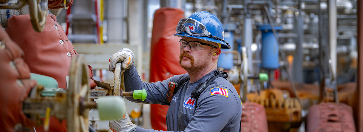 An MPLX employee tightening a wheel on a pipe while smiling